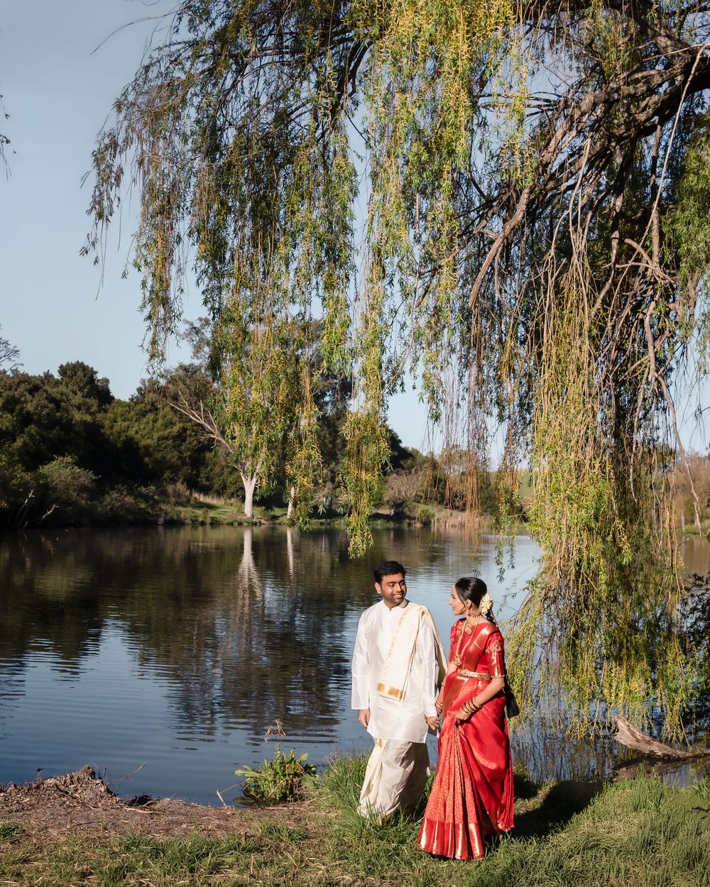 A couple beneath a weeping willow at the edge of a still lake