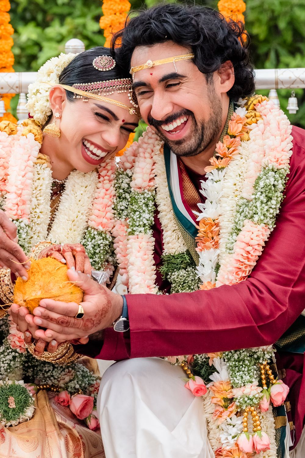 A bride and groom laughing together during the ceremony, heavy in flower garlands