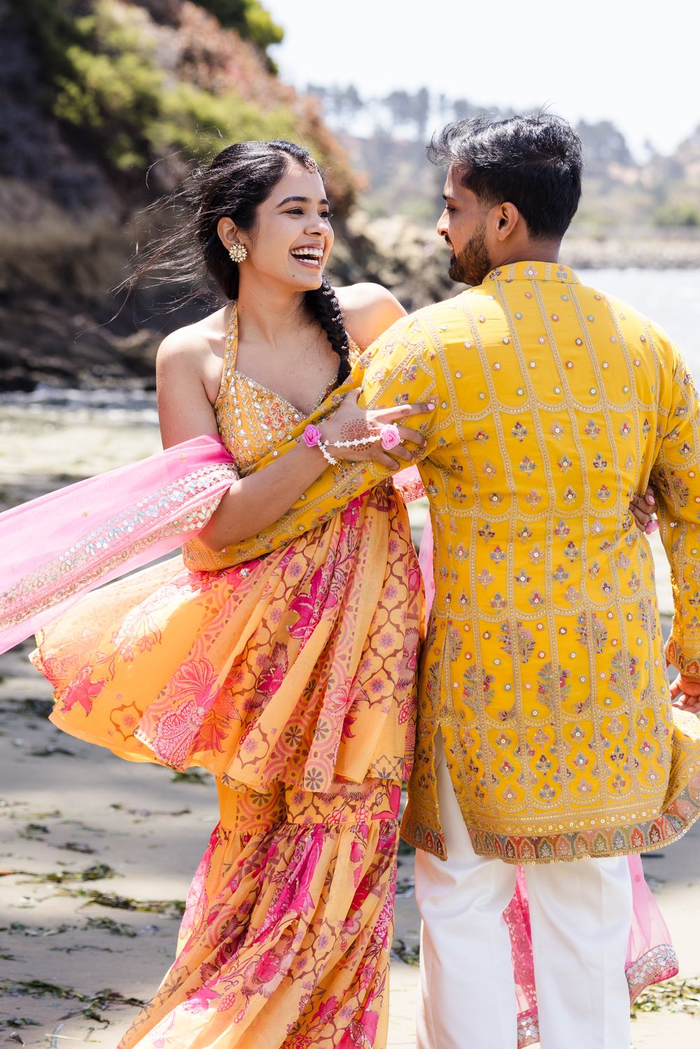 A couple laughing on the beach in yellow and pink, fabric caught in the wind