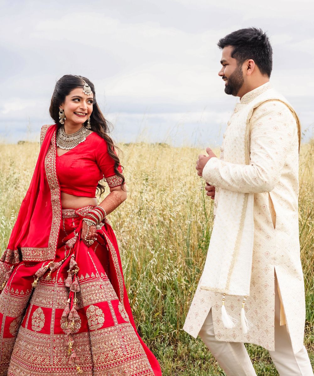 A bride in deep red turning to her groom in a field of tall summer grass